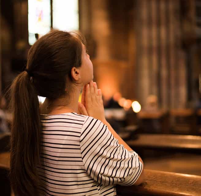 Woman praying with hands together in church, peaceful spiritual moment.