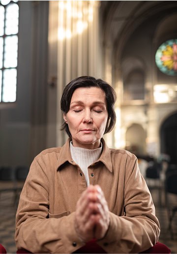 Woman praying with closed eyes in church, serene and peaceful atmosphere.