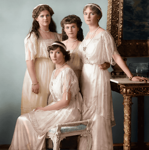 Four girls in vintage dresses with jewelry, posed indoors with a piano and ornate mirror.