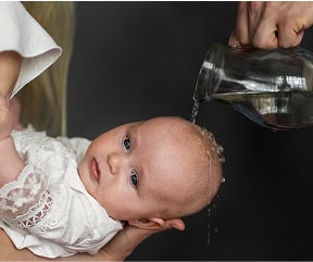 Baby with a bald head being poured water on during a bath or skincare routine.