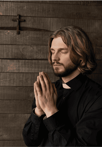 Man in prayer with hands together and eyes closed, religious setting with wooden background.